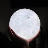 Hand holding a moon-shaped light bulb against a dark background
