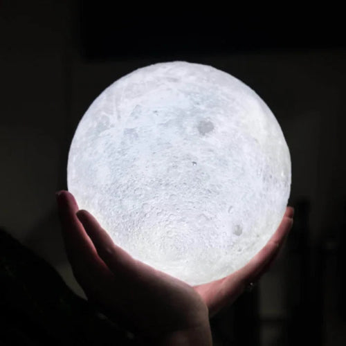Hand holding a moon-shaped light bulb against a dark background